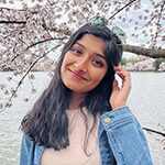 Samidha Sane stands in front of a cherry blossom tree. She smiles and has head tilted and her hand in her hair. on 