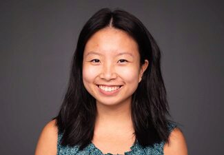 jianwei headshot Headshot of a person with long dark hair smiling against a dark background, wearing a patterned sleeveless top.